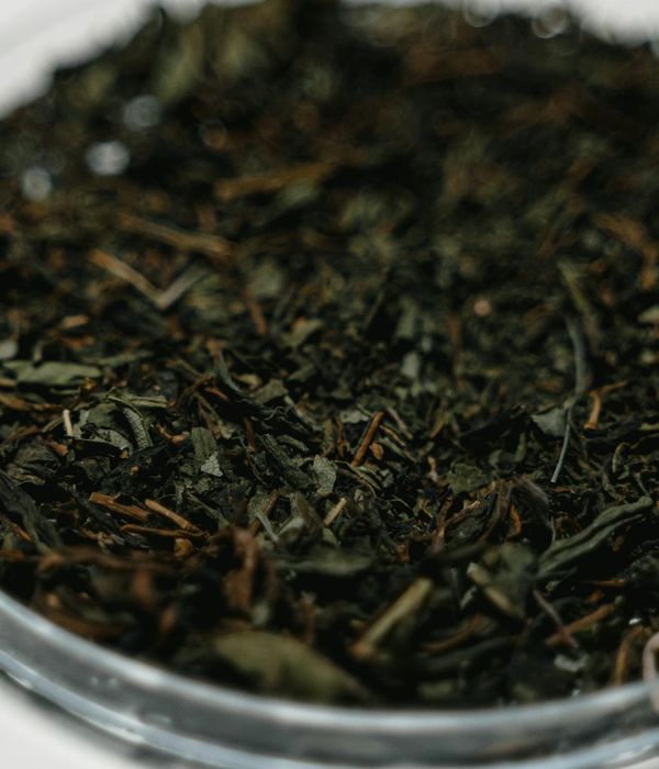 Detailed close-up of green herbal tea leaves in dark bowl